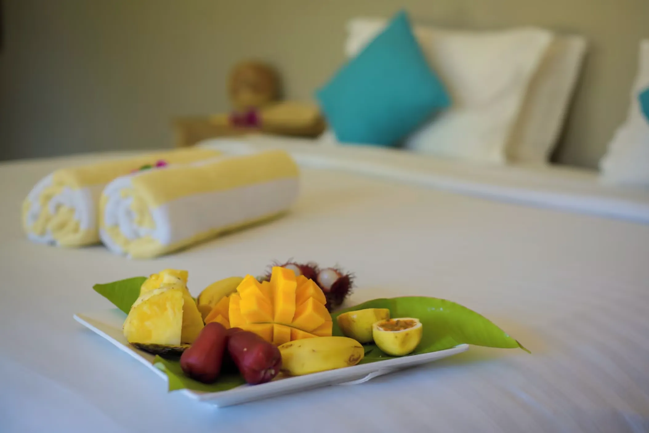 A plate of cut tropical fruit set out on a made bed in one of the rooms.